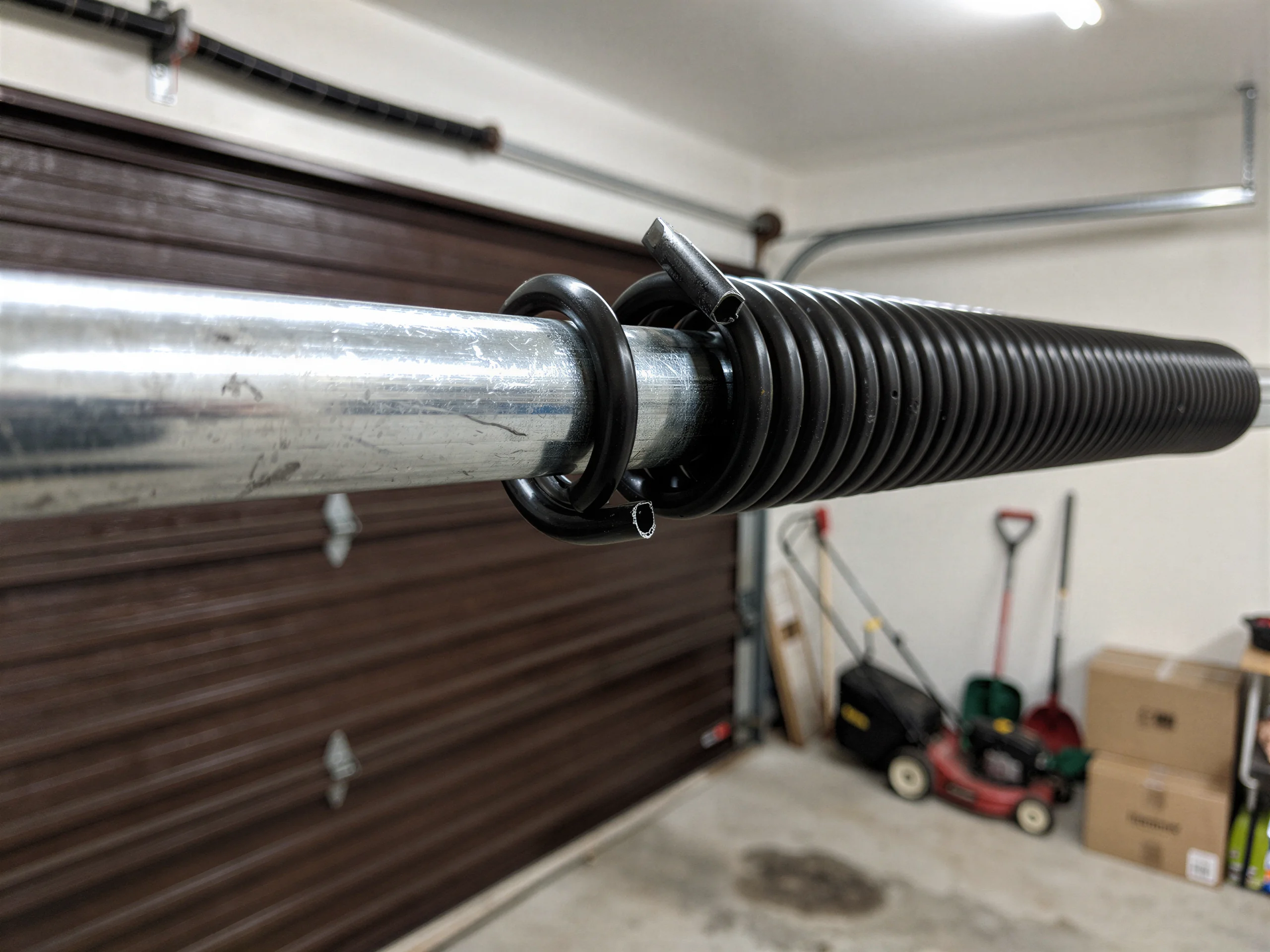 A broken torsion spring is on a metal rod above a brown garage door.